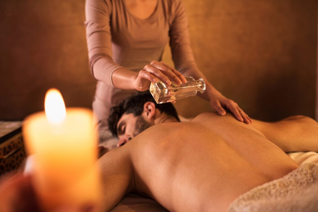 Unrecognizable massage therapist pouring massage oil on man's back